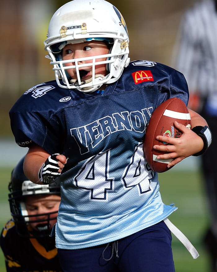 services-03 A young child in football gear holding a ball during a game on the field.