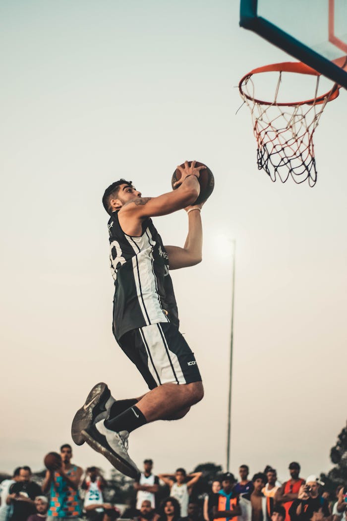 services-04 Athlete gracefully performs a dunk during an outdoor basketball game, showcasing skill and strength.